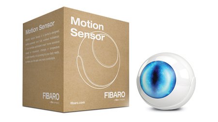 Bílý pohybový senzor Fibaro svítí modře a leží na bílém pozadí s krabičkou.